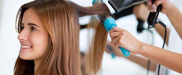 парикмахер вытягивает волосы с помощью фена и брашинга