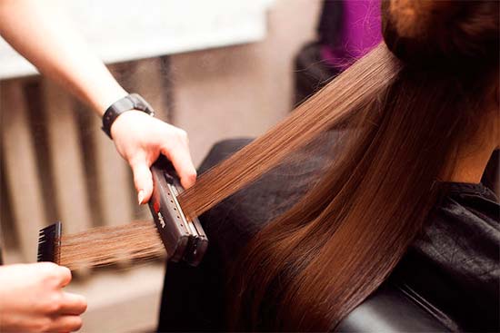парикмахер вытягивает клиентке волосы утюжком